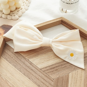 Close-up of cream bow hair clip with daisy embroidery on a wooden tray with decor