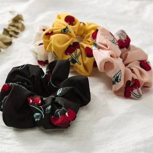 Close-up of three fruit pattern scrunchies in yellow, pink and black on linen cloth