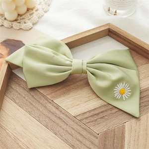 Detail of light green silk bow hair clip featuring delicate white daisy embroidery
