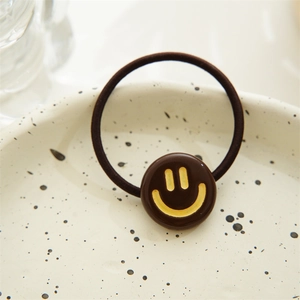 Close-up of a brown elastic hair tie with a yellow smiley face charm on a ceramic tray