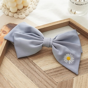 Detail of light blue bow hair clip with daisy embroidery on a wooden aesthetic tray