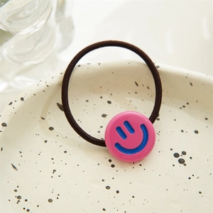 Detail of high-elasticity black hair tie with pink smiley face charm on a textured tray