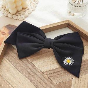 Close-up of black bow hair clip with white daisy embroidery on a wooden tray decor