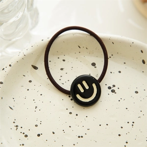 Close-up of a brown elastic hair tie with a black smiley face charm on a ceramic tray