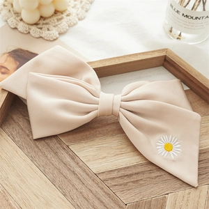 Detailed close-up of beige bow hair clip with white daisy embroidery on a wooden tray