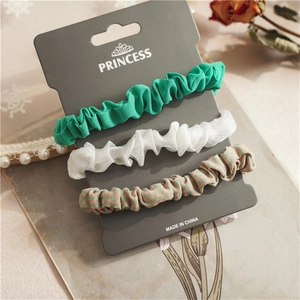 Close-up of green, white chiffon and plaid hair scrunchies on a branded card packaging