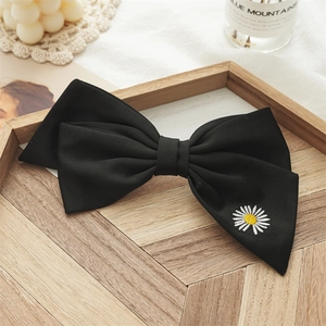 Close-up of black bow hair clip featuring detailed white daisy embroidery on matte fabric