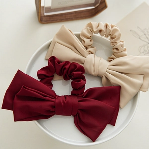 Detailed macro view of burgundy and beige satin double-layered bow scrunchies on white tray