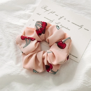 Close-up of pink scrunchie with red cherry print and soft fabric texture on white background