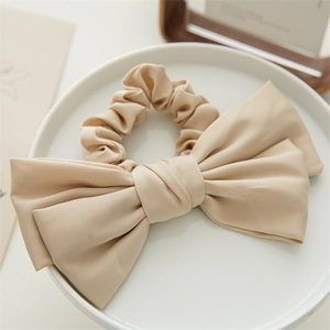 Detail view of large beige satin double-layered bow scrunchie on a decorative white plate
