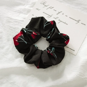 Close-up of black fabric scrunchie with red cherry print on white linen background