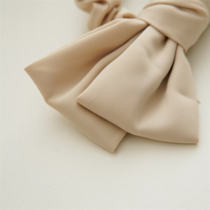 Detail of elegant beige satin double bow hair tie with smooth matte texture and pleats