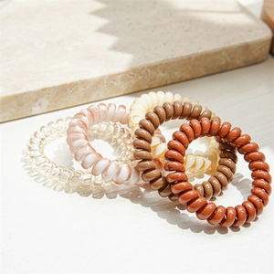 Close-up of five spiral hair ties in earth-toned colors on a clean marble surface