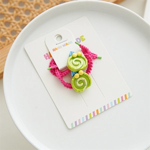 Detailed view of handmade pink elastic hair tie with green swirl charms on a white card