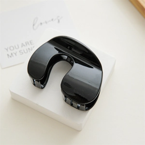 Close-up of a large glossy black U-shaped shark hair clip on a white stone pedestal