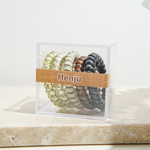 Close-up of four spiral hair ties in olive, beige, amber, and black in a clear box