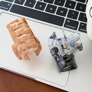Detailed view of two acetate hair claws with marble textures on a modern laptop background