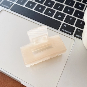 Macro view of cream apricot rectangle hair claw with marble texture on laptop