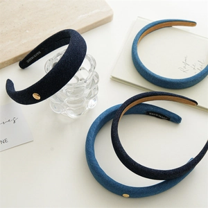 Détail du serre-tête en jean bleu avec design rembourré et ornement logo en métal doré
