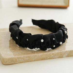 Detail of black pleated satin headband with white pearl accents on marble surface