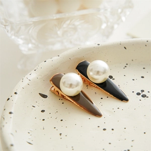 Close-up of minimalist pearl hair clips in black and coffee finish on a ceramic tray