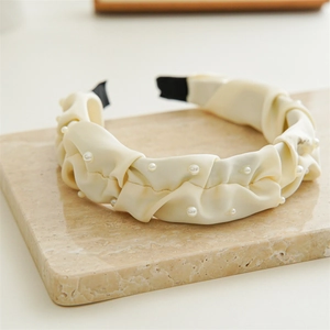 Detail of cream pleated satin headband featuring delicate white pearls and elegant texture