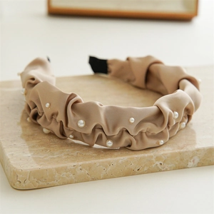 Detail of coffee-colored pleated satin headband with white pearls on a marble base