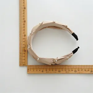 Elegant beige fabric headband with white pearls and measurement tool on white background