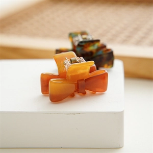 Mini acetate bow hair clips in amber and tortoise shell patterns on a white stand