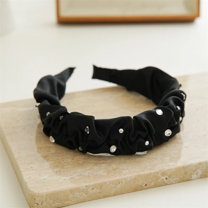 Close-up of black pleated satin headband with sparkling rhinestones on stone display