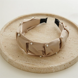 Close-up of pleated apricot fabric headband with white pearls on a stone tray