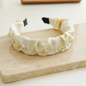 Detail of cream pleated satin headband featuring elegant sparkling clear rhinestones