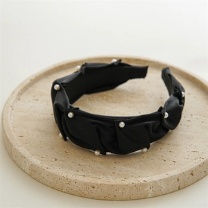 Close-up of black ruched satin headband with white pearls on a beige stone tray