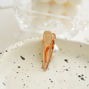 Detailed close-up of a high-quality gold metal duckbill hair clip on a ceramic tray