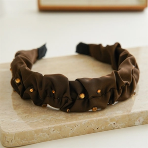 Detail of coffee-colored pleated satin headband with amber rhinestones on stone surface