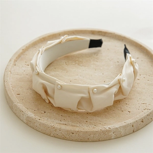 Detailed view of the layered folds and small white pearls on the elegant beige headband