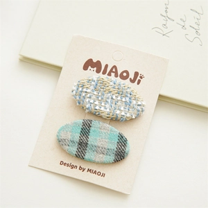 Détail de deux barrettes en tissu avec textures en tweed bleu et carreaux sur carte cadeau