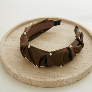 Detail of brown pleated satin headband with delicate white pearl accents on stone tray