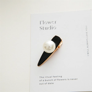 Detail shot of an elegant water-drop hair clip with a large pearl and black enamel finish