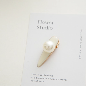 Detail of cream enamel hair clip with white faux pearl on golden metal base