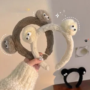 Gros plan de serre-têtes en peluche douce avec grands yeux et pompons poilus en trois couleurs