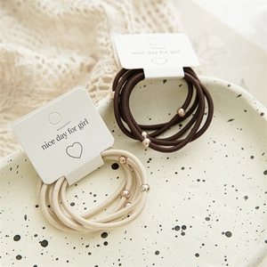 Detailed macro of minimalist hair ties with gold beads on beige ceramic tray display