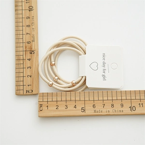 Minimalist beige elastic hair ties with gold beads set shown on measuring scale
