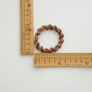 Detailed view of 5cm brown braided hair tie with mini pom-poms and oval fastener
