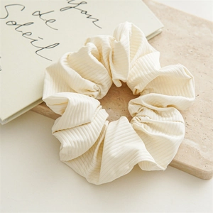 Detailed close-up of a cream-colored ribbed fabric scrunchie on an elegant marble stand