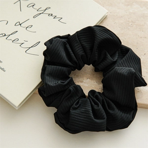 Close-up of black ribbed fabric scrunchie on beige stone background for elegant hair styling