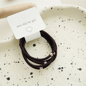 Detail of high-elasticity dark brown hair ties with gold and silver beads on a display card