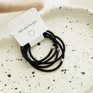 Close-up of black elastic hair bands with gold metal beads on a heart paper card