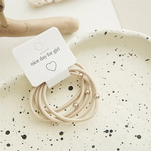 Detailed view of beige elastic hair ties with rose gold beads on display card