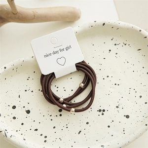 Detail of three brown elastic hair ties with gold beads on a white display card